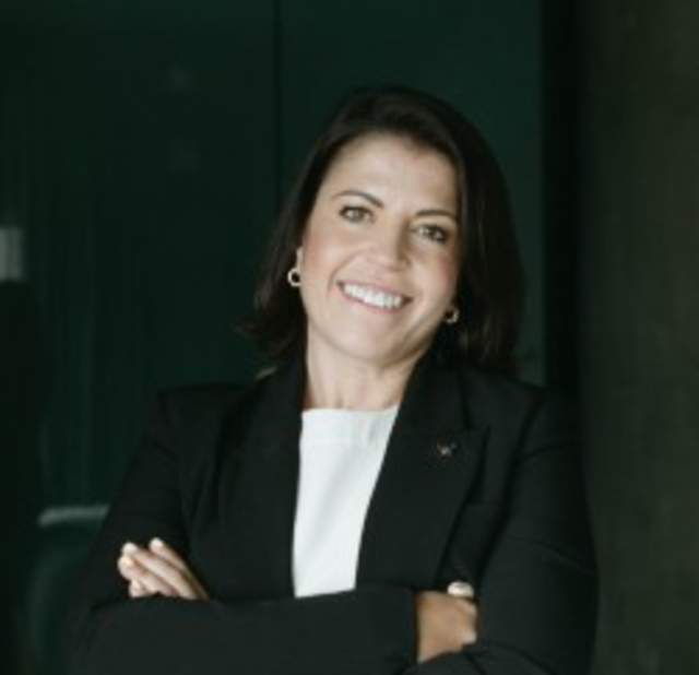 A woman wearing a black blazer smiling into the camera posing for a headshot.