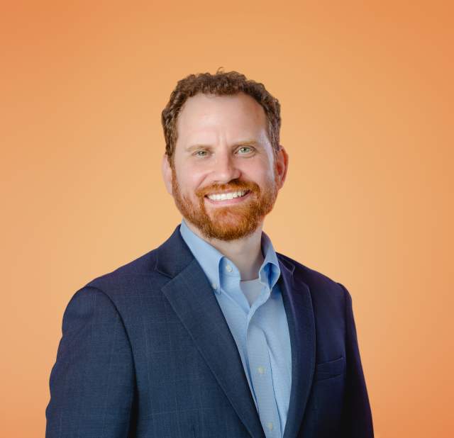 Jeremy Martin smiling and posing for a headshot against an orange background.