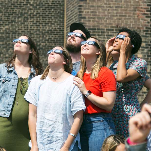 Group of people wearing safety glasses looking into sky for eclipse