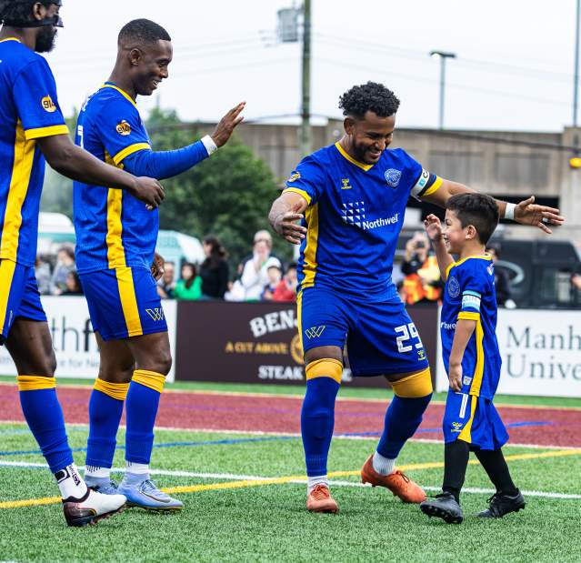 A group of three Westchester Soccer players high five a junior player.