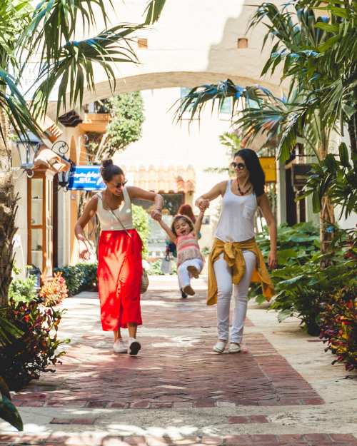 two women holding hands with a child as they swing her along a palm beach family resort walkway