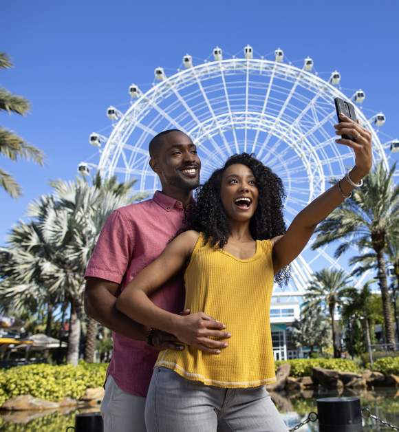 A couple posing for a selfie in front of The Wheel at ICON Park