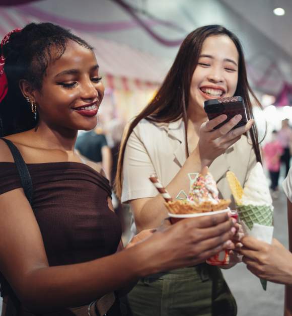Happy girlfriends capturing a photo of their ice cream in the city at night.