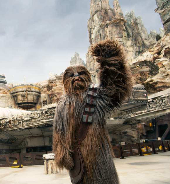 Disney's Hollywood Studios. Chewbacca waving at Star Wars: Galaxy’s Edge, with the Millennium Falcon and towering rock formations in the background.