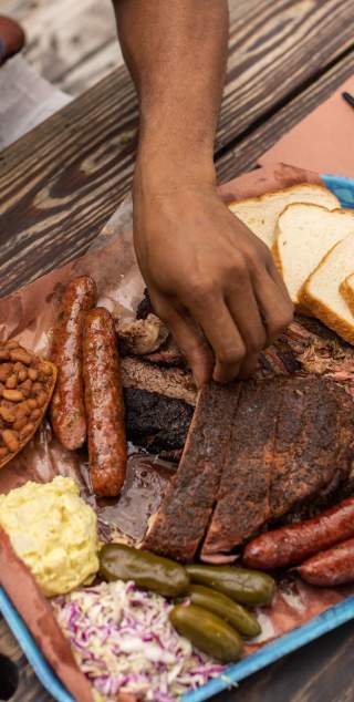 Plastic tray covered in butcher paper topped with slices of different barbecue meats and traditional sides.