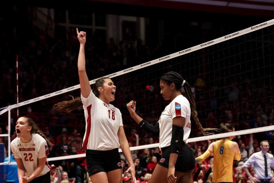 A UW-Madison women's volleyball player points one finger in the air after a point while her teammate fist pumps the air next to her at the net.