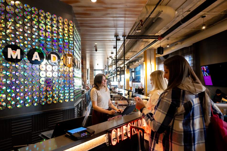 Two hotel guests check in with smiling front desk worker at The Moxy