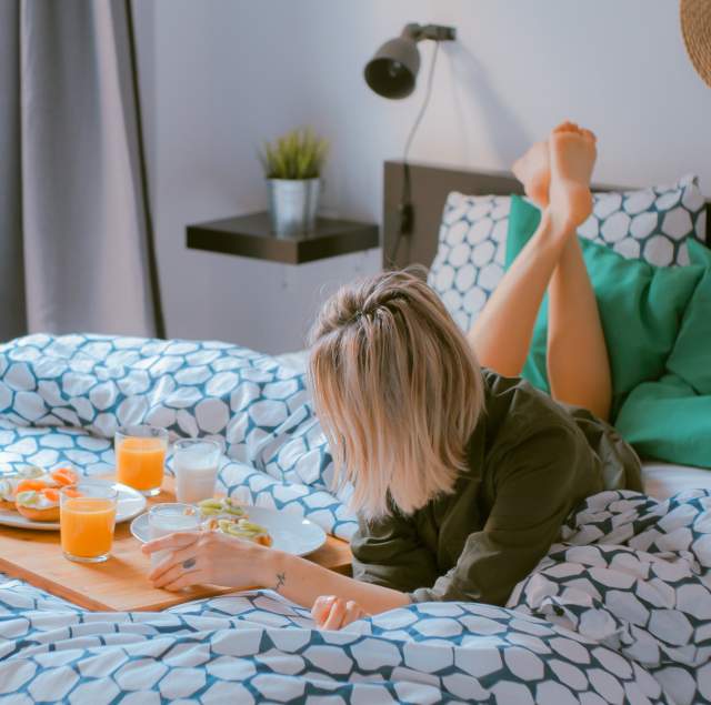 Woman-laying-down-on-hotel-bed-having-breakfast