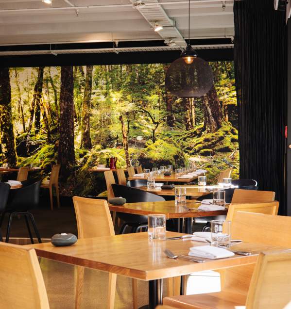 Interior view of Rata Restaurant with modern wooden tables and chairs and a large forest decal on the back wall