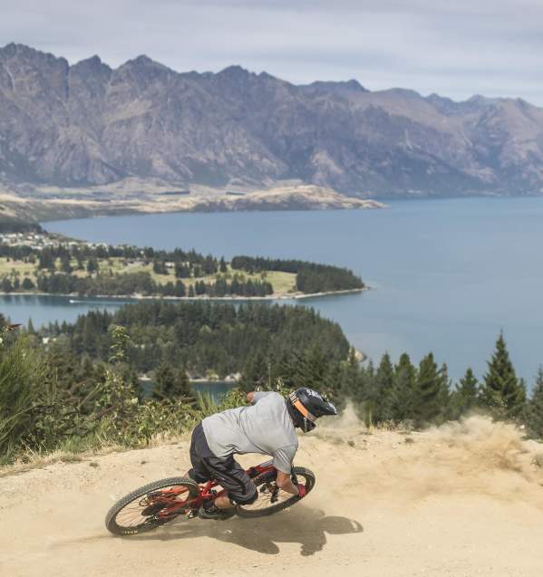 Person biking Queenstown Bike Park with view overlooking lake Whakatipu and the Remarkables mountain ranges