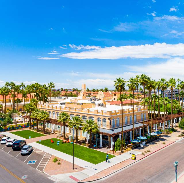 Aerial of Crowne Plaza Phoenix-Chandler Golf Resort showing an two-story hotel with many palm trees surrounding the property and blue sky with clouds above