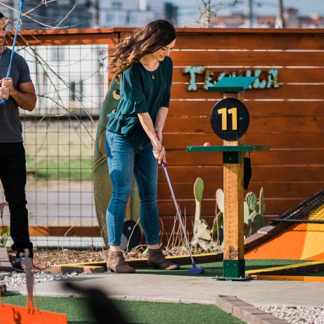 Three people playing putt-putt golf at a bar in San Marcos, TX