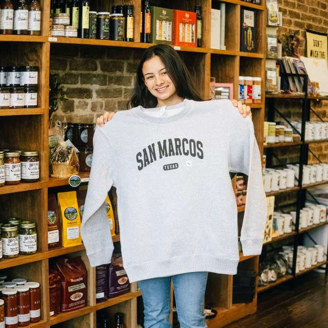 Rae Tinney poses with a San Marcos sweater at The San Market in Downtown San Marcos, Texas