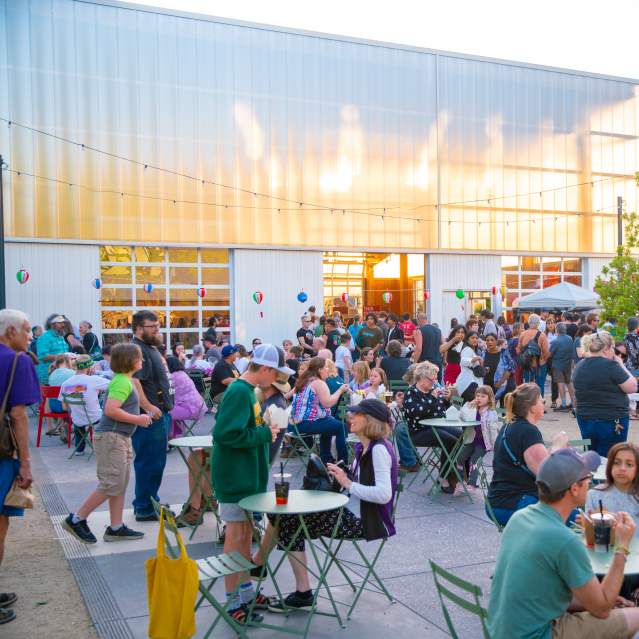People gather outside at tables to eat and talk at twilight.