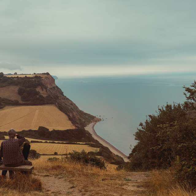 two people sitting on a bench overlooking sidmouth