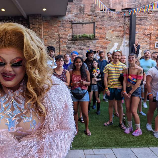 A drag queen in pink feathers and a shiny top with a crowd behind her