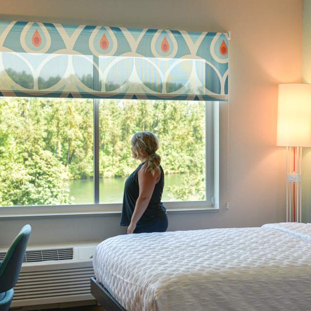 A woman looks out a window in a bright, clean hotel room