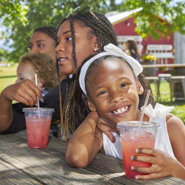 A girl at a picnic table smiles with her pink lemonade.
