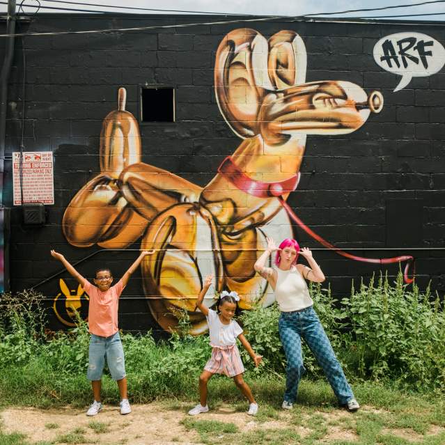 Woman and two kids pose in front of a mural in Downtown San Marcos, TX.