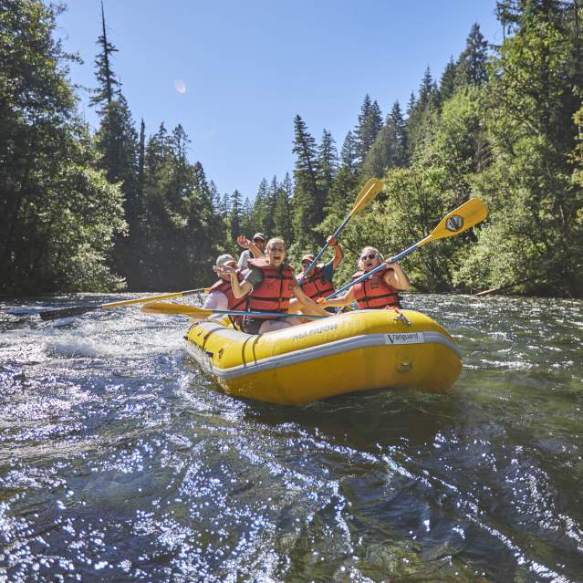 A yellow river raft full of happy rafters floats down the river