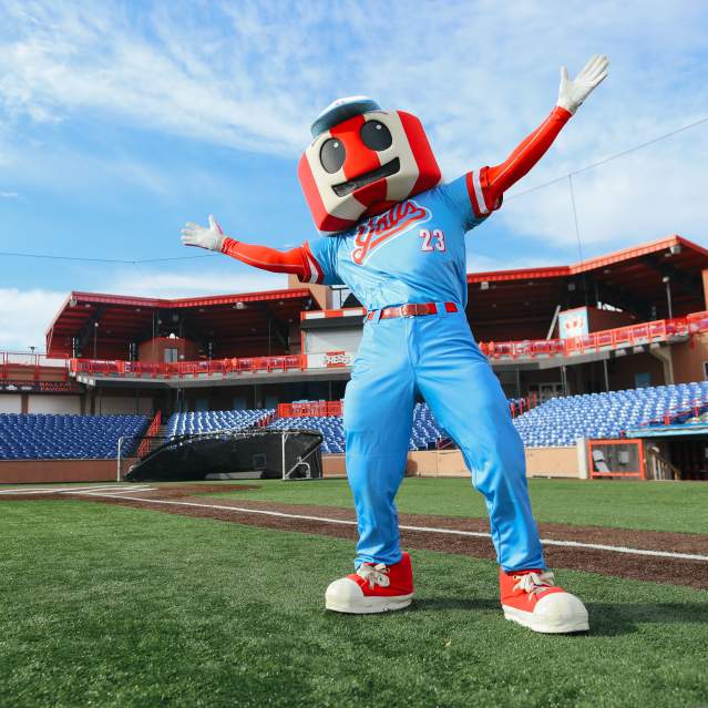 A red and white striped water tower mascot in a blue uniform stretches its arms wide with stadium seating behind.