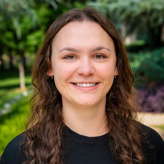 Headshot of Bailey Hall with brunette hair and a black shirt with trees in the background