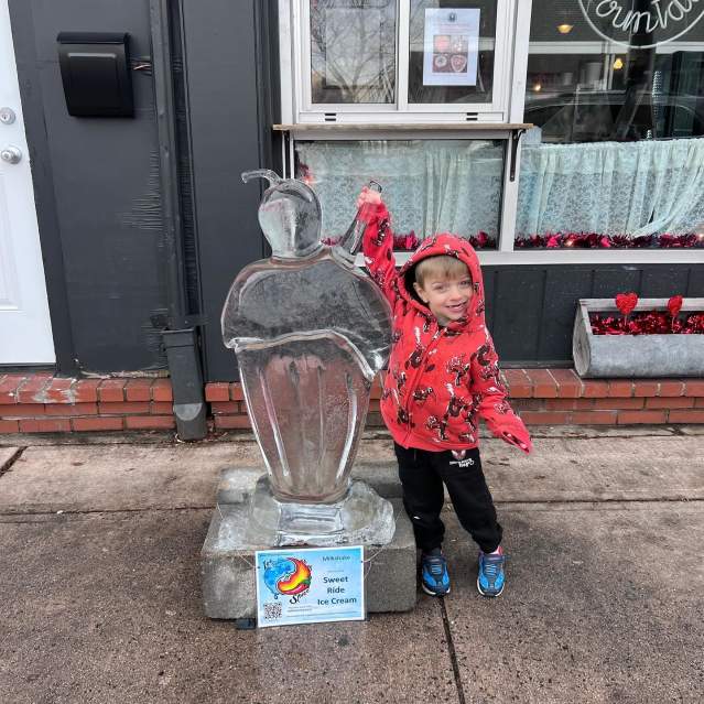 Child stands with ice sculpture of an ice cream sundae at the ice and spice festival.