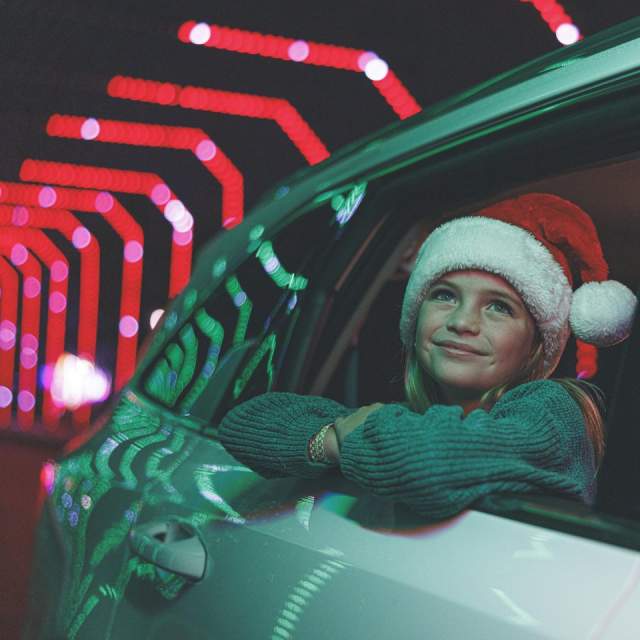 A young girl wearing a Santa hat looks out a car window at a festive drive-through Christmas light display during a holiday vacation in Branson, Missouri