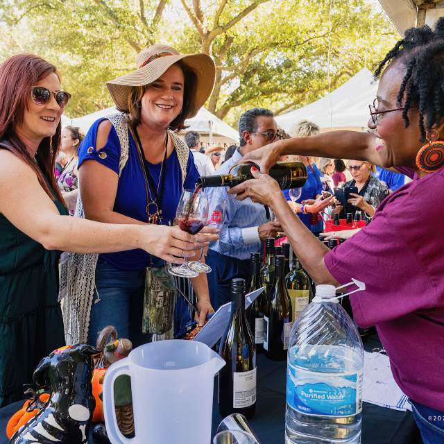 two women hold up wine glasses to be filled at rouge et blanc festival