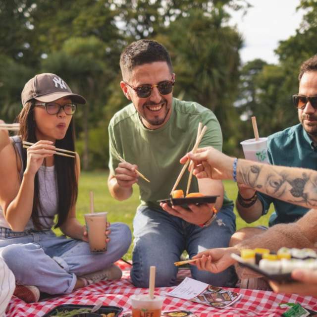 Group of friends enjoying sushi and bubble tea on a picnic blanket in the park