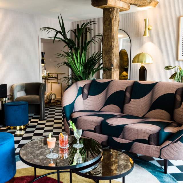 Three cocktails on a table in a stylish cocktail lounge with bold-print sofa and checkered floor at The Old Stocks Inn in the Cotswolds