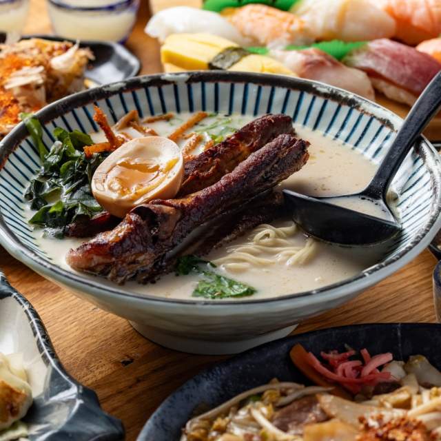 Spread of Japanese cuisine on wooden table including big bowl of ramen, dumplings, and sushi