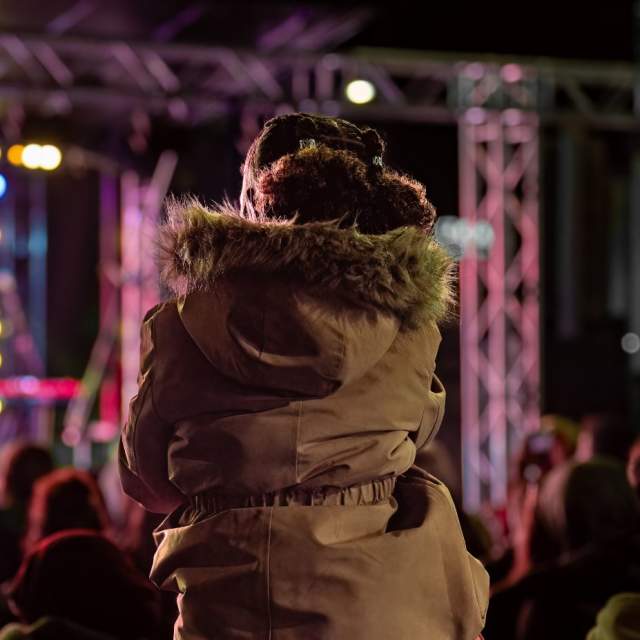 Girl sitting on man's shoulders to see guitarist on stage at Countdown to Christmas event