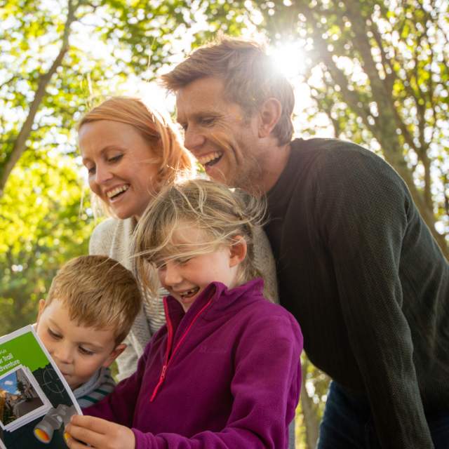 A smiling family look at a treasure trail leaflet in a woodland