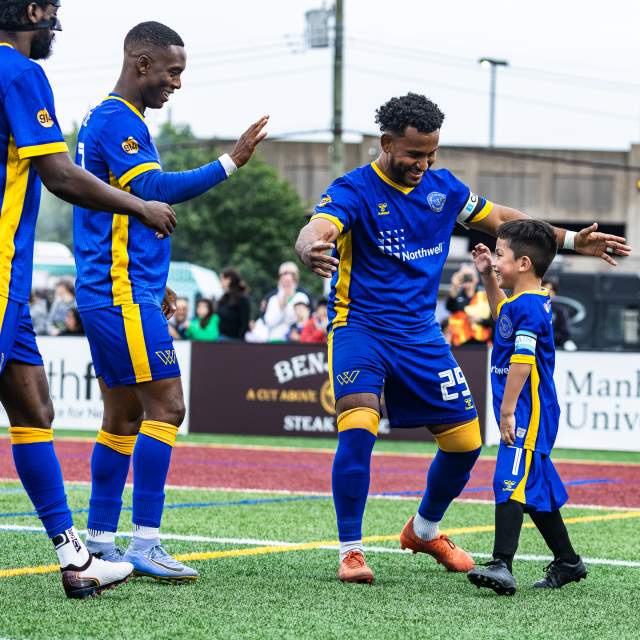 A group of three Westchester Soccer players high five a junior player.