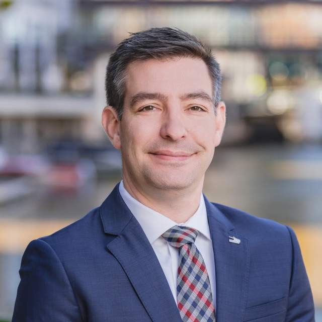 Matt Dorner in a navy suit, with a blue and red crosshatched tie, smiling in a headshot.