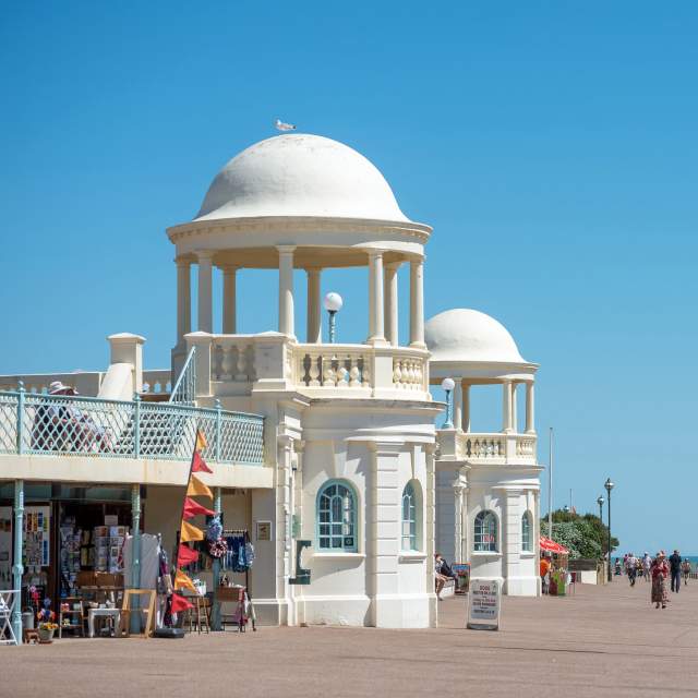 A sunny day in Bexhill on the promenade, with white cafe buildings and shops