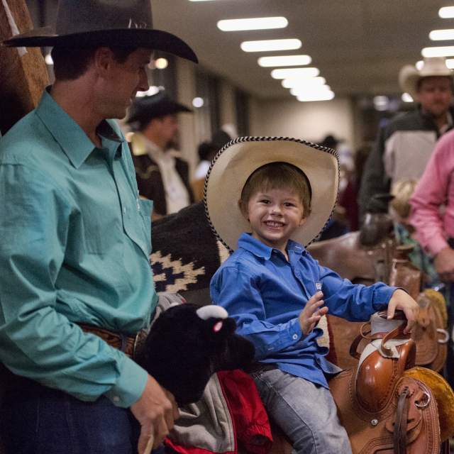 young boy smiling wearing a cowboy hat in a crowd of people