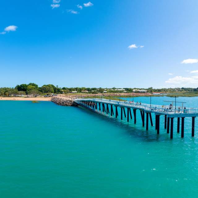 People walking along and fishing from Town Beach Jetty in Broome; the image is taken from the water, looking back along the length of the jetty.
