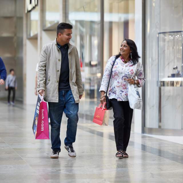 Two people walking towards camera inside Westquay Shopping Centre holding shopping bags and smiling