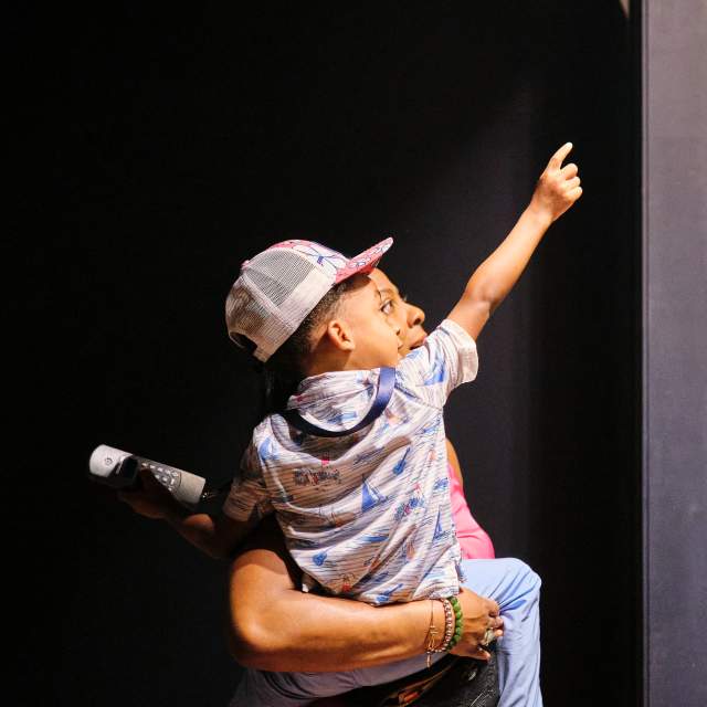 African American man holding a young child in front of the plaque with engraved names of the Clotilda, the Last American Slave Ship