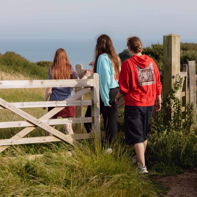 A group of 3 young people walking through a gate towards the sea on the Sussex Downs