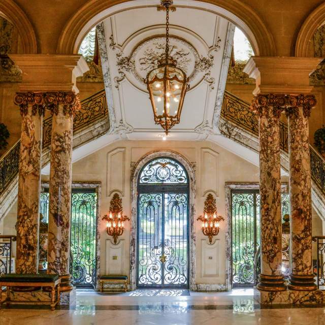 A luxurious lobby with marble columns, a chandelier, and ornate details.