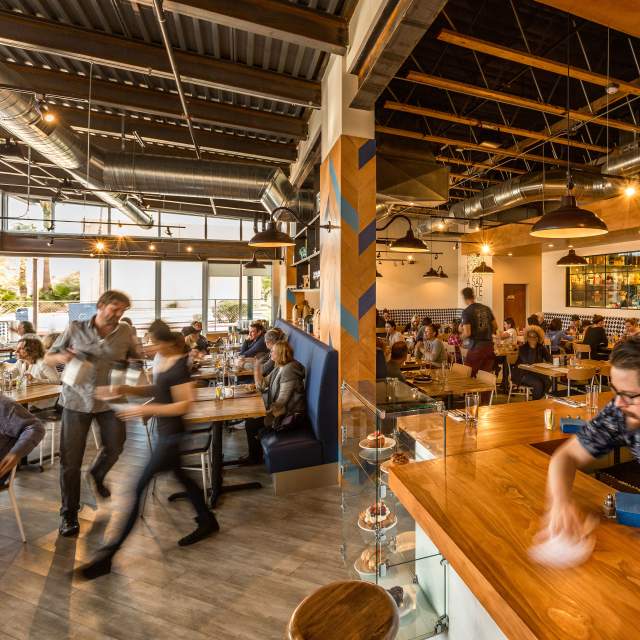 Man wiping down counter in the corner inside of a busy restaurant. bright morning sun and natural tones with wood detailing