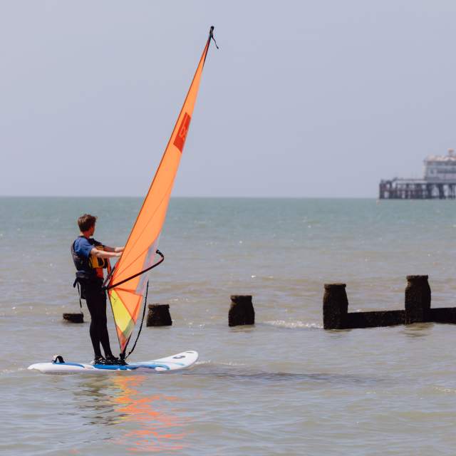 Windsurfer with orange sail looking at the pier on the Sussex coast