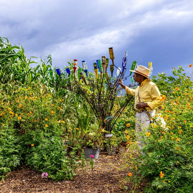 Man stands next to an abstract sculpture in a flourishing garden