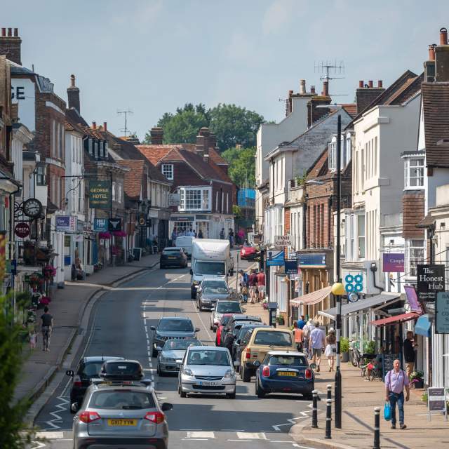 A busy high street with traffic in the historic town of Battle, Sussex, with shop fronts and shoppers