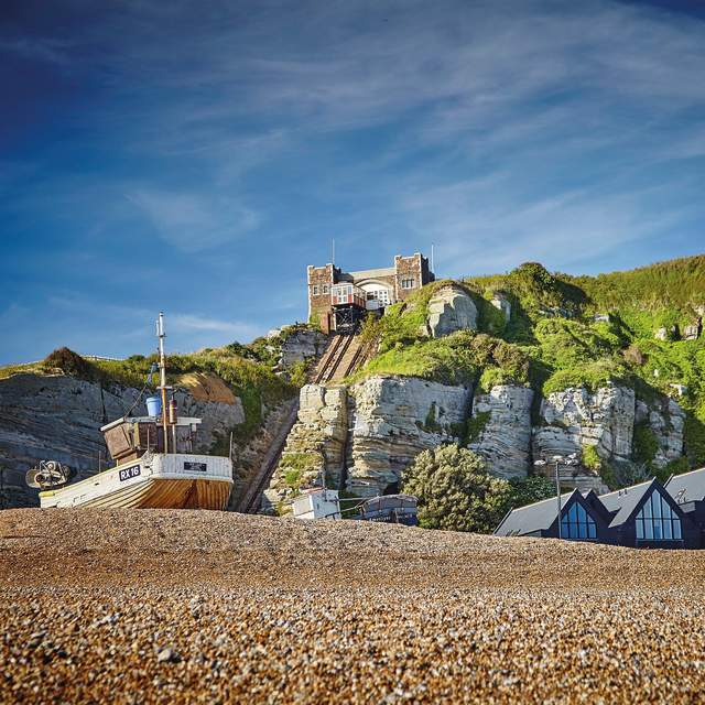 Shingle beach and fishing boat in Hastings Old Town, with cliffside lift in the background