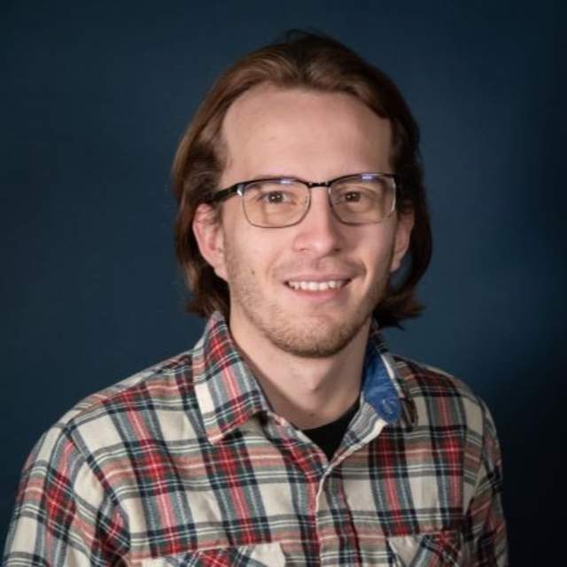 Man wearing glasses and a plaid shirt poses for a picture