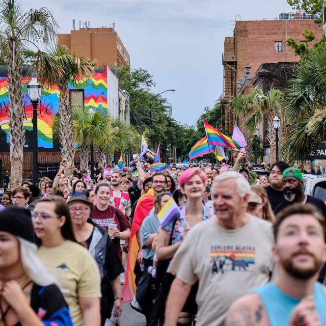 Group of people celebrating Pride in the street with rainbow flags in background